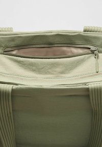 Világoszöld szövet táska belseje cipzáras zsebbels, textúrált anyaggal és pliszírozott pánt részletekkel. Puha felület, semleges béléssel.