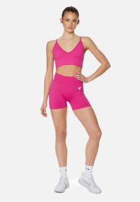 Upravený športový outfit v jasne ružovej farbe, ktorý obsahuje skrátenú športovú podprsenku s nastaviteľnými ramienkami a šortky s vyšším pásom, oboje vyrobené z elastického materiálu.