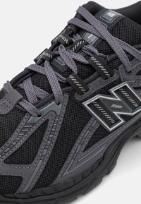 Chaussure de course New Balance noire et grise avec tissu mesh, couture détaillée, lacets à motifs et semelle épaisse texturée.