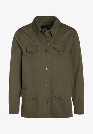 Olivengrøn bomuldsjakke med knaplukning foran, to brystlommer og to nederste lommer. Har en klassisk krave og metalaccenter.