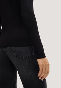 Czarny long-sleeve top o teksturowanym wykończeniu, w połączeniu z ciemnoszarymi dżinsami z klasycznym wzorem kieszeni i lekkim przetarciem.