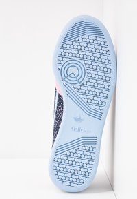 Modrá gumová podrážka s texturovaným vzorem, růžové prvky a tmavý horní design s puntíky, na kterém je logo Adidas.