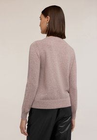 Pulover tricotat roz deschis cu guler rotund, mâneci lungi și tiv ribbit. Textură moale, siluetă ajustată, purtat cu pantaloni negri.