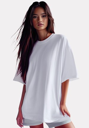 Overmaat wit katoenen T-shirt met korte mouwen, ronde hals en een gladde textuur. Casual gedragen over lichtgekleurde shorts.
