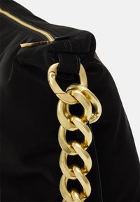 Svart väska med en guldkedjespänne och dragkedja. Mjukt material med en slät yta och en strukturerad form. Gyllene detaljer förbättrar designen.