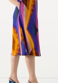 Farbenfrohes Kleid mit geometrischen Mustern in Lila, Orange und Gelb. Der Stoff wirkt glatt, hat eine mittlere Länge und seitliche Taschen.