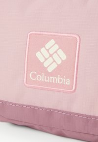 Vaaleanpunainen kangaspussi, jossa on rosoinen pinta ja valkoinen Columbia-logo vaaleanpunaisella taustalla, joka on korostettu ommellulla reunalla.