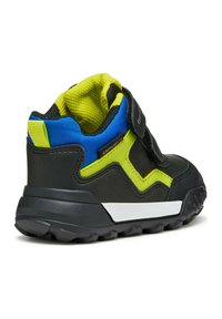 Zapatilla deportiva negra y gris con acentos en verde neón y azul, parte superior texturizada, cinta de Velcro, suela gruesa y cuello acolchado.