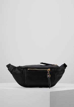 Sac banane en cuir noir avec une finition texturée, quincaillerie en zipper doré et une étiquette amovible, présentant une forme incurvée avec une sangle ajustable.