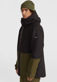 Veste isolante noire et verte avec capuche, fermeture éclair à l'avant, poignets réglables et accents de logo sur la poitrine et la manche.