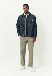 Denim jacket with front pockets, a button closure, and contrasting collar; paired with a navy top and light beige pants and white sneakers.