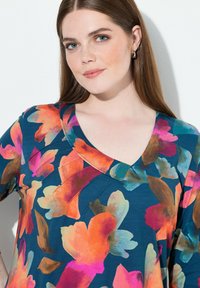 Top a stampa floreale con scollatura a V profonda, base blu e tonalità vivaci di arancione, rosa e verde in un tessuto morbido.