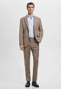 Jasnobrązowy garnitur o dopasowanym kroju, zestawiony z jasnoniebieską koszulą wizytową. Czarnych butów dopełniają stylizację, przedstawioną na neutralnym tle.