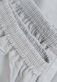 Tejido elástico gris claro con textura fruncida y detalles de costura contrastantes, mostrando una vista en primer plano de la cinturilla.