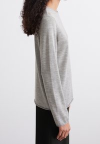 Pull gris clair à manches longues avec un col rond et une texture lisse et douce. Présente une coupe droite et un ourlet légèrement arrondi.