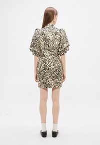 Sukienka w panterkę z krótkimi bufkowatymi rękawami, strukturalną sylwetką i fakturowaną tkaniną w beżowo-czarnych odcieniach, długość do kolan.