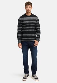 Sort og grå stribet striktrøje med rund halsudskæring, parret med mørkeblå jeans og sorte sneakers med hvide såler.