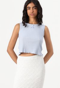 Top cropped azul claro com ribbing texturizado e bordas em forma de onda, apresentando um pequeno laço no decote. Saia branca texturizada.