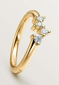 Anillo de oro con un diseño de banda abierta que cuenta con cuatro diamantes de corte redondo engastados en garras, dispuestos de forma asimétrica en un lado.