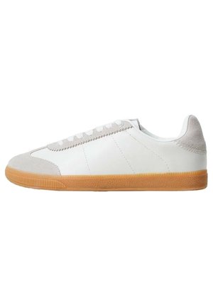Biały niski sneaker z jasnoszarymi zamszowymi wstawkami na palcach i pięcie, białymi sznurowadłami oraz brązową gumową podeszwą.