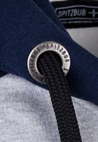 Navy stof met een grijs gebied, voorzien van een metalen oogje met het label "SPITZBUB" en een gestructureerde zwarte sneakerschoenlace die erdoorheen is geweven.