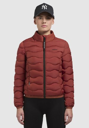 Rode puffy jack met een golvende doorgestikte ontwerp, zwarte rits, hoge kraag en elastische manchetten. Gecombineerd met een zwarte honkbalpet.