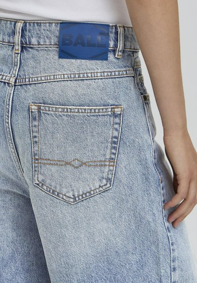 Jeans en denim bleu clair avec une poche arrière visible, présentant des coutures contrastantes et une pièce en cuir bleu étiquetée "BALL."