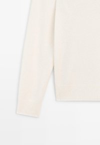 Maglione color crema realizzato in morbido tessuto a maglia. Presenta maniche lunghe, polsini a coste e una vestibilità leggermente rilassata.