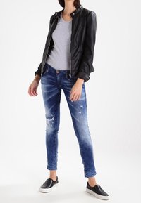 Černá kožená bunda, šedé tričko, modré oprané džíny a černé slip-on tenisky. Jednoduchý outfit s různými texturami a barvami.