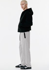 Sort hættetrøje, grå sweatpants med sidelukning som accent, og sorte sneakers med hvide detaljer, vist på en model.