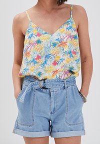 Camisole en soie à motifs floraux avec un col en V, présentant des motifs tropicaux jaunes, bleus et roses. Assortie à un short en denim clair taille haute, avec des revers roulés.