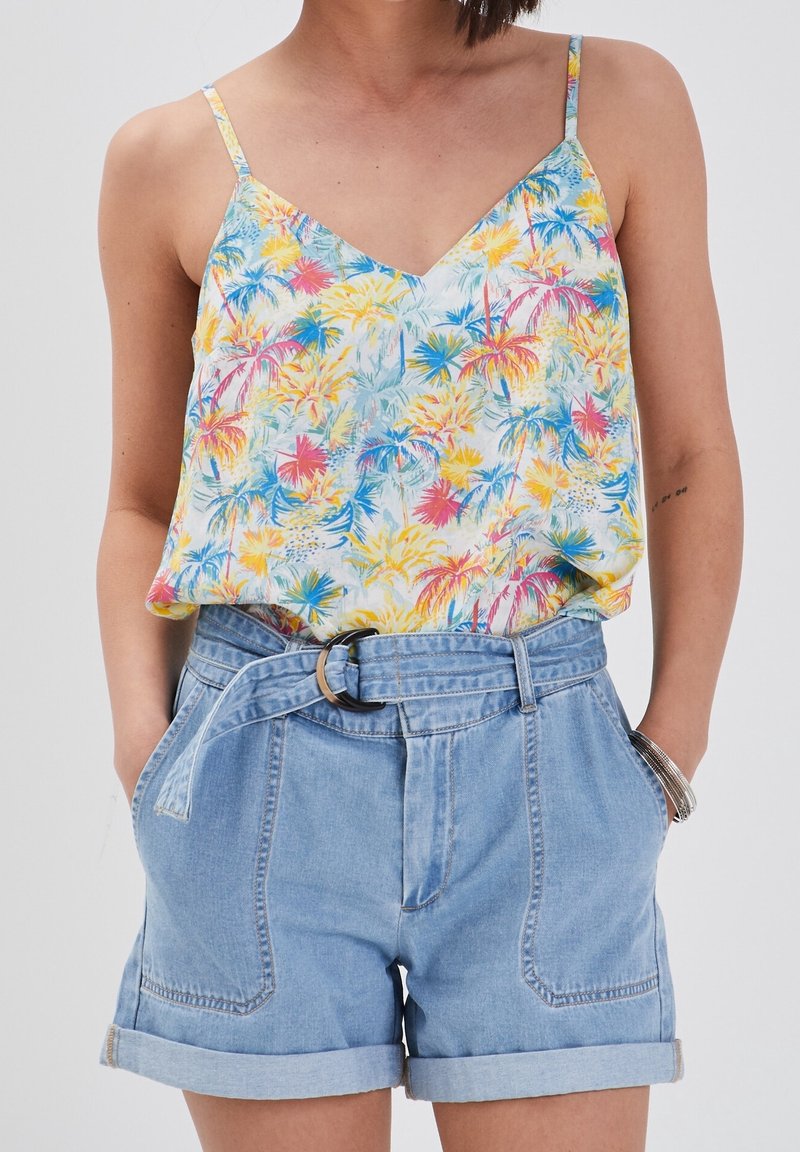 Camisole en soie à motifs floraux avec un col en V, présentant des motifs tropicaux jaunes, bleus et roses. Assortie à un short en denim clair taille haute, avec des revers roulés.