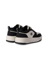 Schwarze und cremige Sneakers mit einer strukturierten Oberseite, runden Zehen, dicke Sohle und kontrastierenden Logoakzenten an der Ferse und an der Seite.