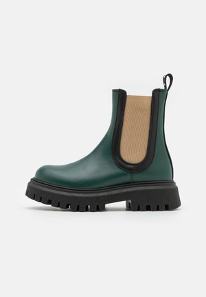 Bota Chelsea de couro verde com acabamentos pretos, painel lateral elástico, sola preta robusta e padrão de ranhura texturizado. Apresenta uma alça na parte de trás.