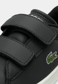 Sneaker nera sintetica con due strappi in Velcro, caratterizzata da una finitura testurizzata e un piccolo logo di coccodrillo verde sul lato.