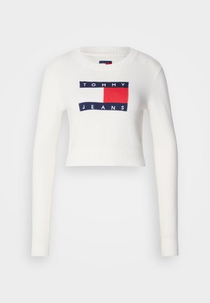 Hvid cropped sweater med lange ærmer; har et strikket logodesign i marineblå og rød inden i en rektangulær lap på forsiden.