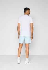 Camisa de homem de manga curta azul clara combinada com calções azul claro e sapatilhas brancas, vista pela parte de trás. Tecido suave, design casual.