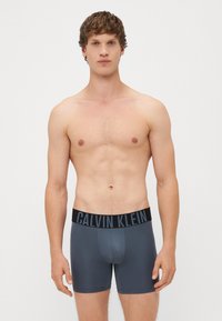 Boxer in grigio realizzati in tessuto liscio, dotati di una vita elastica nera con il logo "CALVIN KLEIN". Design aderente e a vita media.