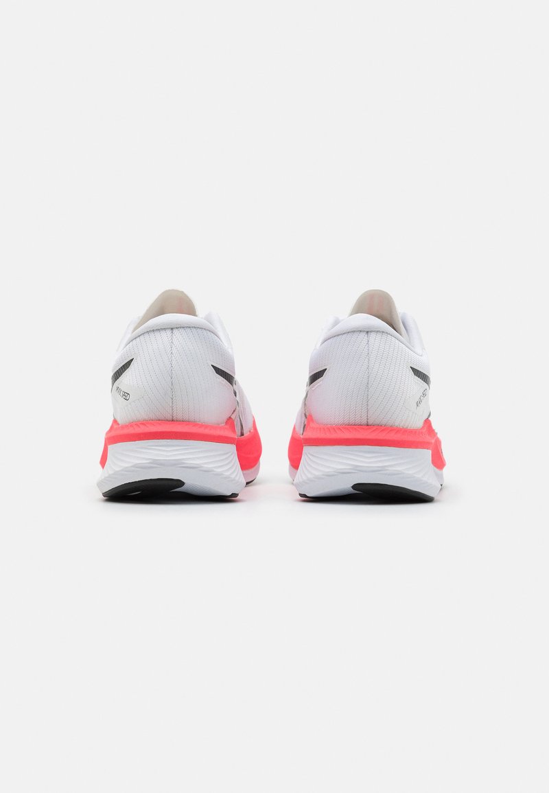Des chaussures de sport blanches avec un dessus en maille texturée, présentant un accent rose au niveau du talon, une semelle noire et des détails réfléchissants à l'arrière.