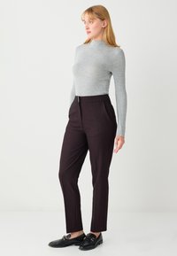 Haut gris à manches longues associé à un pantalon taille haute bordeaux foncé, avec un design épuré et un accent métallique à la taille. Des mocassins noirs complètent le look.