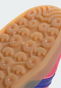 Suela de zapato de goma con un patrón de relieve texturizado y circular. Los colores incluyen melocotón y naranja con un acabado suave y características de diseño distintas.
