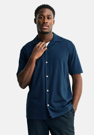 Marineblå kortærmet skjorte med camp-krave, hvide knapper, glat stof og en afslappet pasform, kombineret med bukser med pindstriber.