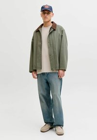 Veste vert olive avec col marron, t-shirt beige, jean bleu clair et chaussures beiges sans lacets ; style décontracté, coupe ample et design minimaliste.
