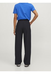 Högmidjade svarta byxor med vida ben, gjorda av ett slätt tyg, har en bakficka och är i kombination med en blå kortärmad skjorta.