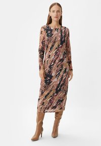 Langärmliges, gemustertes Kleid in Rosa-, Braun- und Schwarztönen; transparente Stoff mit fließendem Design, kombiniert mit kniehohen beigen Stiefeln.