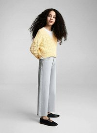 Gul stickad tröja med V-ringning, kombinerad med högmidjade ljusblå vida jeans och svarta snörskor. Texturerad, avslappnad outfit.