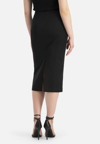Jupe crayon noire avec fente arrière, texture lisse et design ajusté. Assortie à des escarpins noirs à lanières autour de la cheville.
