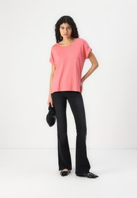 Coral pink short-sleeve top with a relaxed fit, paired with black flared pants and black slip-on shoes, holding a black clutch bag.