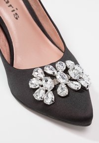 Chaussure noire à bout pointu ornée sur le devant d'un grand groupe de strass clairs en forme de goutte d'eau.