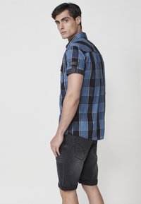 Blauw en zwart geruit korte mouwen shirt met opgerolde mouwen, gecombineerd met donkergrijze shorts met een achterzak detail en een casual pasvorm.